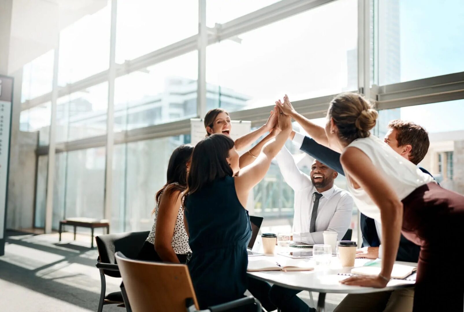 A group of colleagues celebrating with a high-five in a bright office.