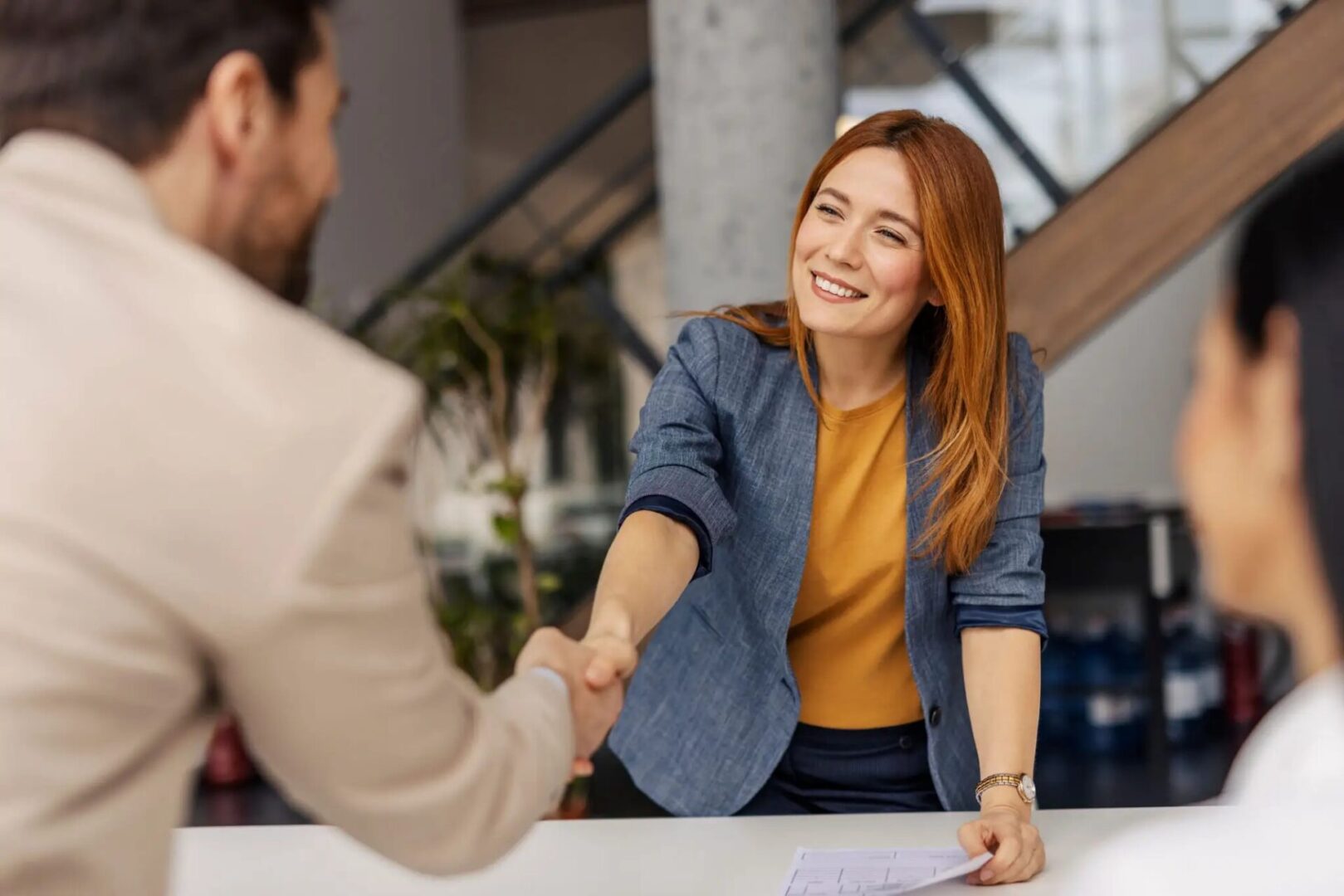 A woman warmly shaking hands with a man in a professional setting.